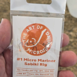 A packet of The Micro Mariner micro fishing sabiki rig, featuring six tiny hooks, alternating colored beads, and durable monofilament lines, neatly packaged on a cardboard line holder with a swivel and snap